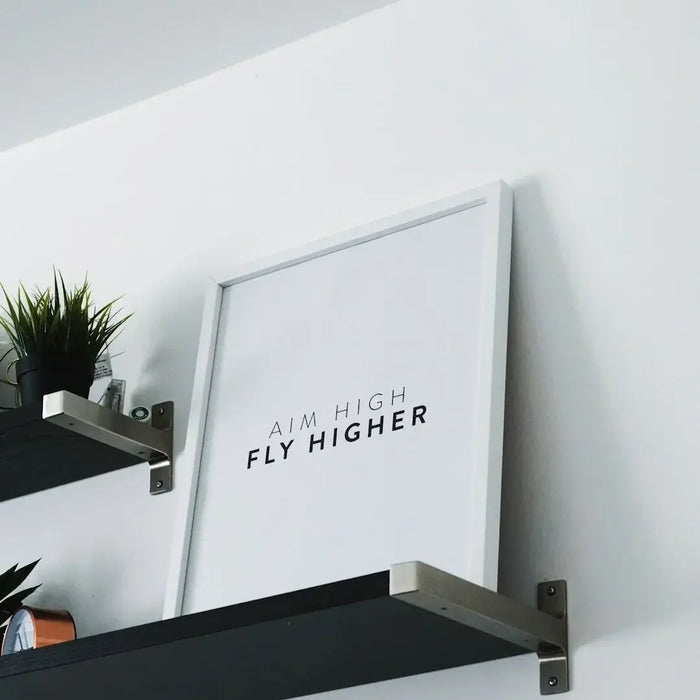 Framed motivational print saying FLY HIGHER on a shelf, enhancing interior design solutions.